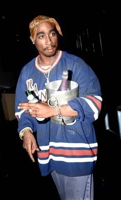 a man in a blue jacket and hat holding a silver bowl with bottles on it