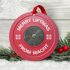 a red christmas ornament hanging from a pine tree with the words merry liftmas from macet on it