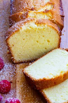 a loaf of pound cake sitting on top of a wooden cutting board next to raspberries