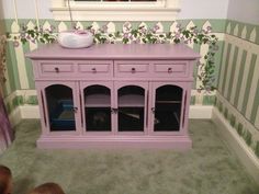 a pink dresser with glass doors and drawers in front of a wallpapered room