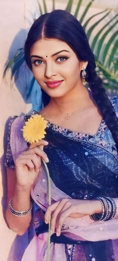 a woman holding a yellow flower in her hand and wearing a blue sari with long braids