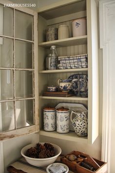 an old window is open to show dishes and other things in the room, including pottery