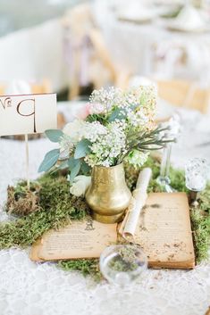 a table topped with an open book covered in moss and flowers next to a small sign