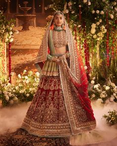 a woman in a red and gold bridal gown standing on a stage with flowers