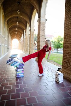 a woman in red jumpsuit kicking books on the ground