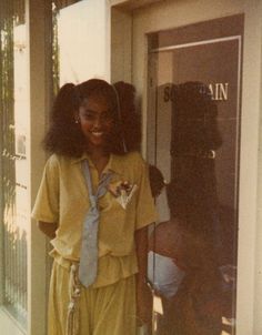 a woman standing in front of a door wearing a yellow shirt and blue neck tie