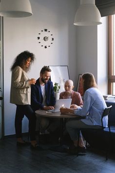 three people sitting at a table with a laptop in front of them and one person standing up