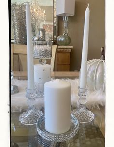 three candles sitting on top of a glass table next to two crystal vases and a mirror