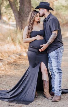 a pregnant woman in a black dress and cowboy hat standing next to a man with his arm around her belly