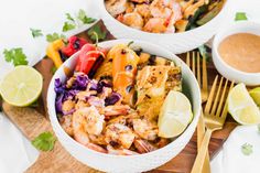 two bowls filled with shrimp and vegetables on top of a wooden cutting board next to a bowl of dipping sauce