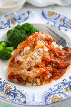 a white plate topped with lasagna covered in sauce and broccoli next to a fork