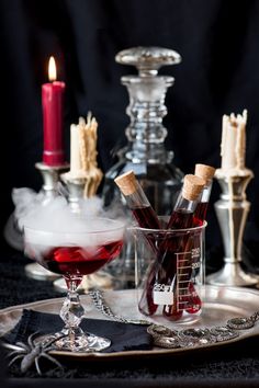 a glass filled with red liquid next to two candles on a plate and another candle holder in the background