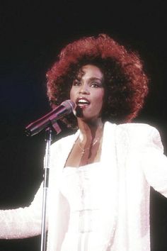 a woman with red hair is singing into a microphone and holding her hands out to the side