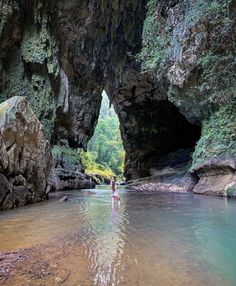 a person wading through a river in the middle of a cave with large rocks on either side