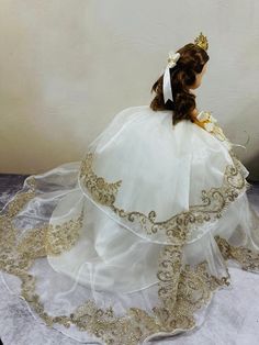 the doll is wearing a white dress with gold trimmings and a tiara