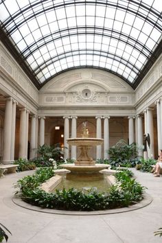 the inside of a large building with a fountain in the center and lots of greenery around it