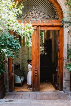 a woman standing at the entrance to a building with an open door and green plants