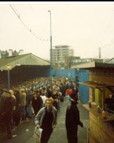 a crowd of people walking down a street next to a blue fence and building with lots of windows