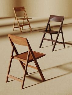 three wooden folding chairs sitting side by side in an empty room with light coming through the window