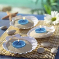 three blue candles sitting on top of plates with seashells and starfish in the background