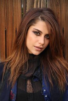 a woman with long hair standing in front of a wooden fence and looking at the camera