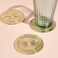 two glass coasters sitting next to each other on a pink surface with a gold rim