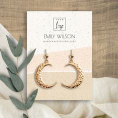 the gold crescent earrings are sitting on top of a white cloth next to a plant