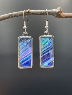 a pair of earrings with blue and purple designs hanging from silver hooks on a tree branch