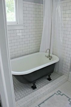 an old fashioned bathtub in a white bathroom with black and gray tile on the floor