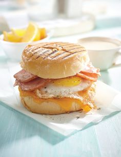 a breakfast sandwich with eggs, ham and cheese on a table next to oranges