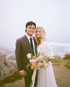 a man and woman standing next to each other in front of the ocean on a cloudy day