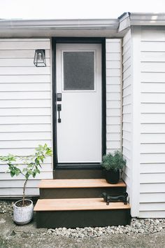 a white door sitting next to a set of steps near a potted plant on the side of a house