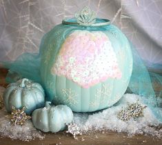 a blue pumpkin decorated with snowflakes and glitters sits on top of some white fluffy balls