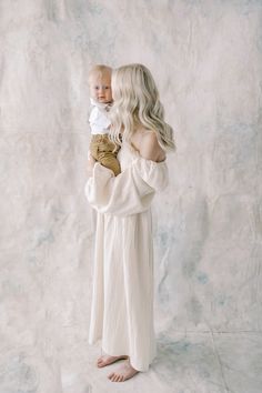 a woman holding a baby in her arms while she is wearing a white dress with long sleeves