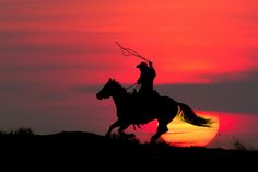 a man riding on the back of a horse in front of a red sky at sunset