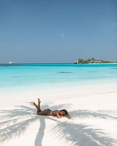 a woman laying in the sand on top of a beach next to palm trees and water