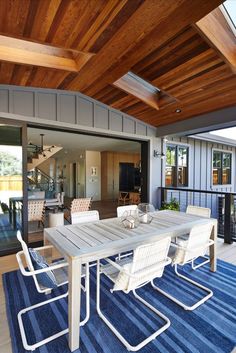 an outdoor dining area with blue and white rugs on the floor, wooden ceiling and sliding glass doors