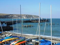 several boats are parked on the beach next to the water with a pier in the background