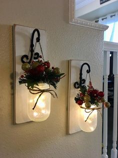 two mason jars with lights are hanging on the wall next to each other, decorated with greenery and flowers