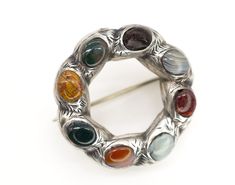 This brooch is a true work of art, crafted from high-quality etched Victorian silver and featuring a combination of Chalcedony, Agate, Jet, and Red Jasper stones. The intricate design of this brooch reflects the Victorian Scottish Celtic style, making it a unique and very rare find. The small round ring design adds a touch of elegance to the piece, and the combination of multi-colored stones creates a stunning contrast against the silver background. Condition: Great vintage condition for its age, there's a chip on a jet stone which I tried to depict (hardly noticeable due to colour), also the clasp most likely was replaced later on. Dimensions: 28mm x 28mm (approx.) Packaging: Our branded suedette Catantica pouch.   Dear buyers, please note that most of our items are pre-owned and might ha Collectible Round Gemstone Brooches, Collectible Round Gemstone Brooch, Antique Jewelry Victorian, Scottish Celtic, Jet Stone, Red Jasper Stone, Scottish Jewellery, Silver Background, Celtic Style