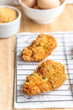 two fried chicken patties on a cooling rack next to some eggs in a bowl