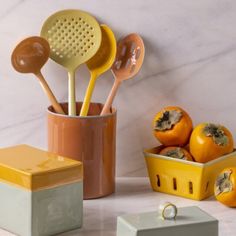 various kitchen utensils are sitting on a counter next to oranges and a yellow container