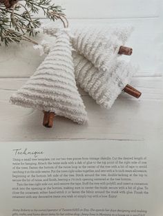 two knitted christmas trees sitting on top of a white wooden table next to a pine branch