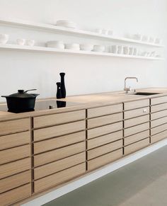 an empty kitchen with wooden cabinets and white dishes on shelves above the sink, along with black pots and pans