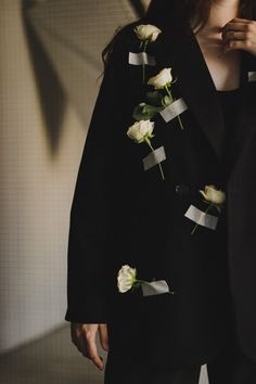 a woman wearing a black jacket with white roses pinned to the lapel and tie