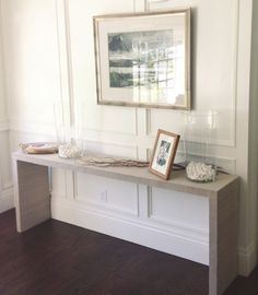 a table with two pictures on it in front of a white wall and wood floor