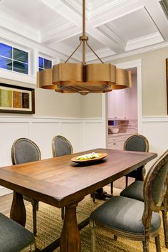 a dining room table and chairs with a bowl of fruit on it in front of the chandelier