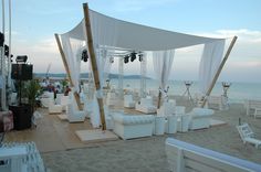 an outdoor wedding setup on the beach with white chairs and draping over it