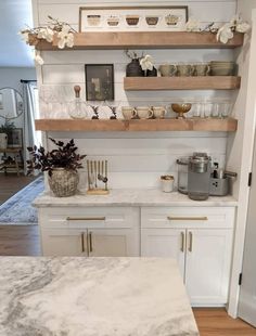 a kitchen with white cabinets and marble counter tops, gold accents on the shelves above