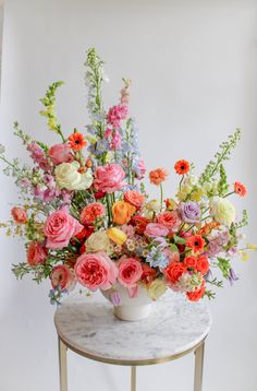 a white vase filled with lots of colorful flowers on top of a marble topped table